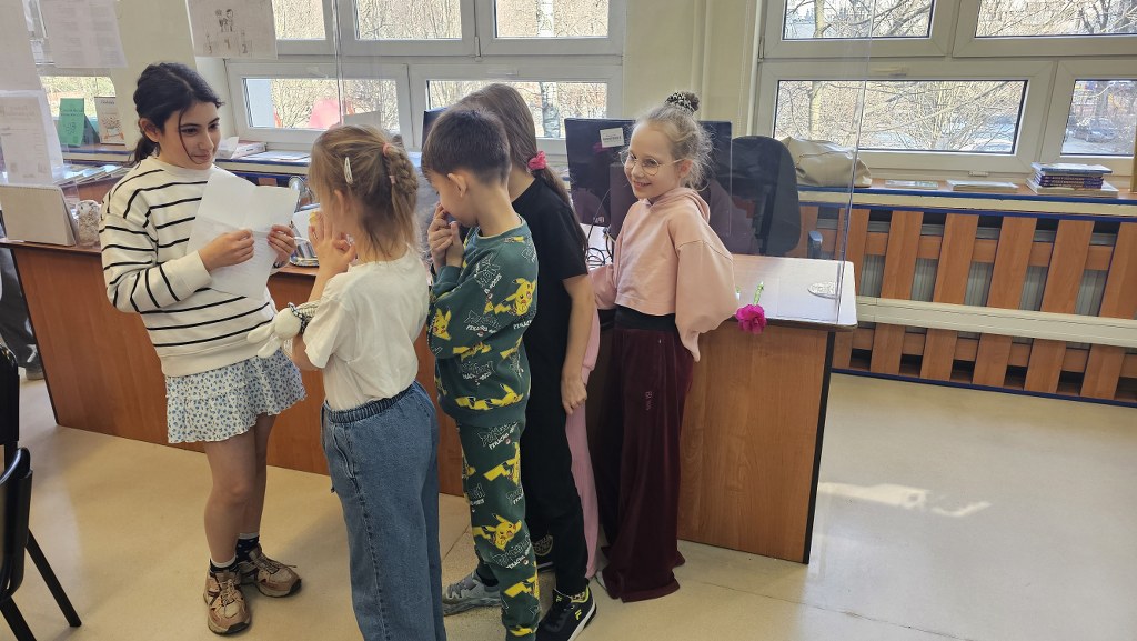 Uczniowie biorą udział w zabawie z zagadkami prowadzonymi przez asystentkę biblioteki szkolnej.